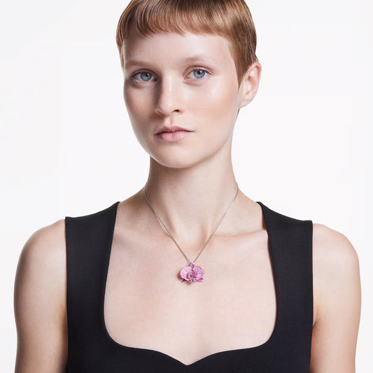 A person with short hair wears a black top and a Swarovski Idyllia Necklace Pendant adorned with pink and white crystals, set against a plain white background.