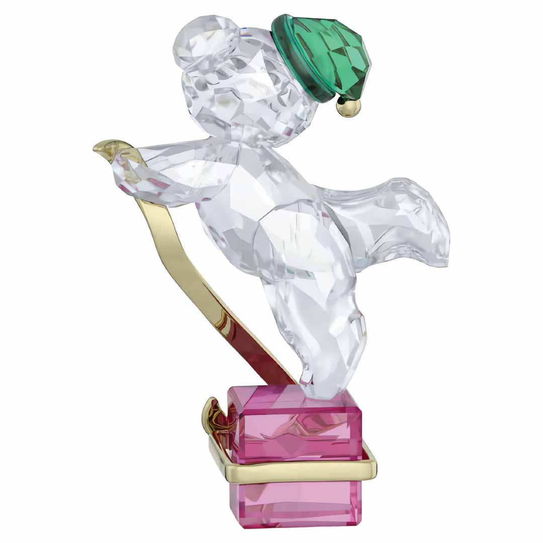 The Swarovski Kris Bear Holiday 2024 Annual Edition by Swarovski is an elegant collectible, featuring the bear in a skiing position with a green hat and golden skis atop a pink and gold base.