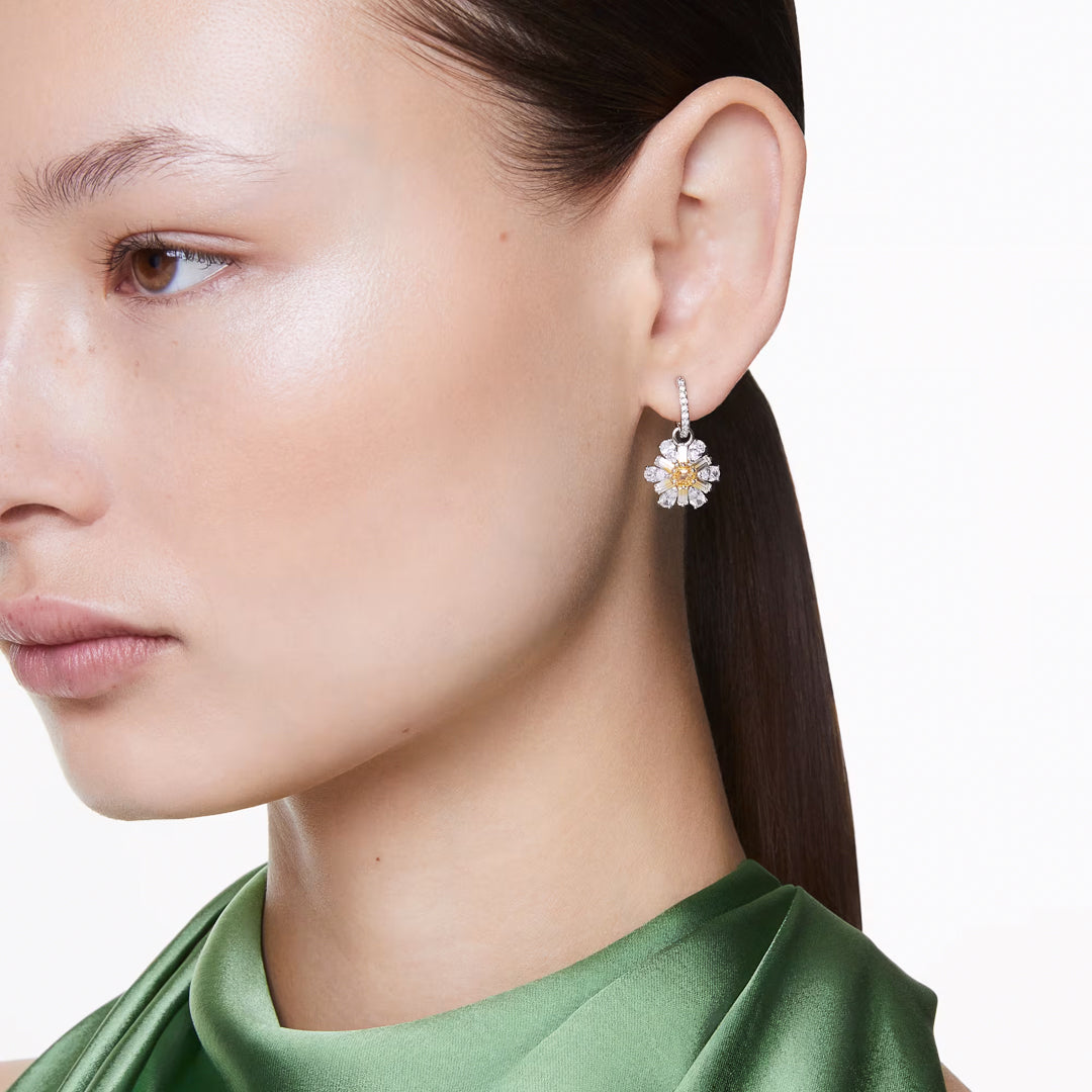 A woman stylishly pulls her hair back against a plain white backdrop, wearing a green satin top and the sparkling Swarovski Idyllia Drop Earrings by Swarovski, elegantly adorned with clear Swarovski Zirconia in a floral-themed design.