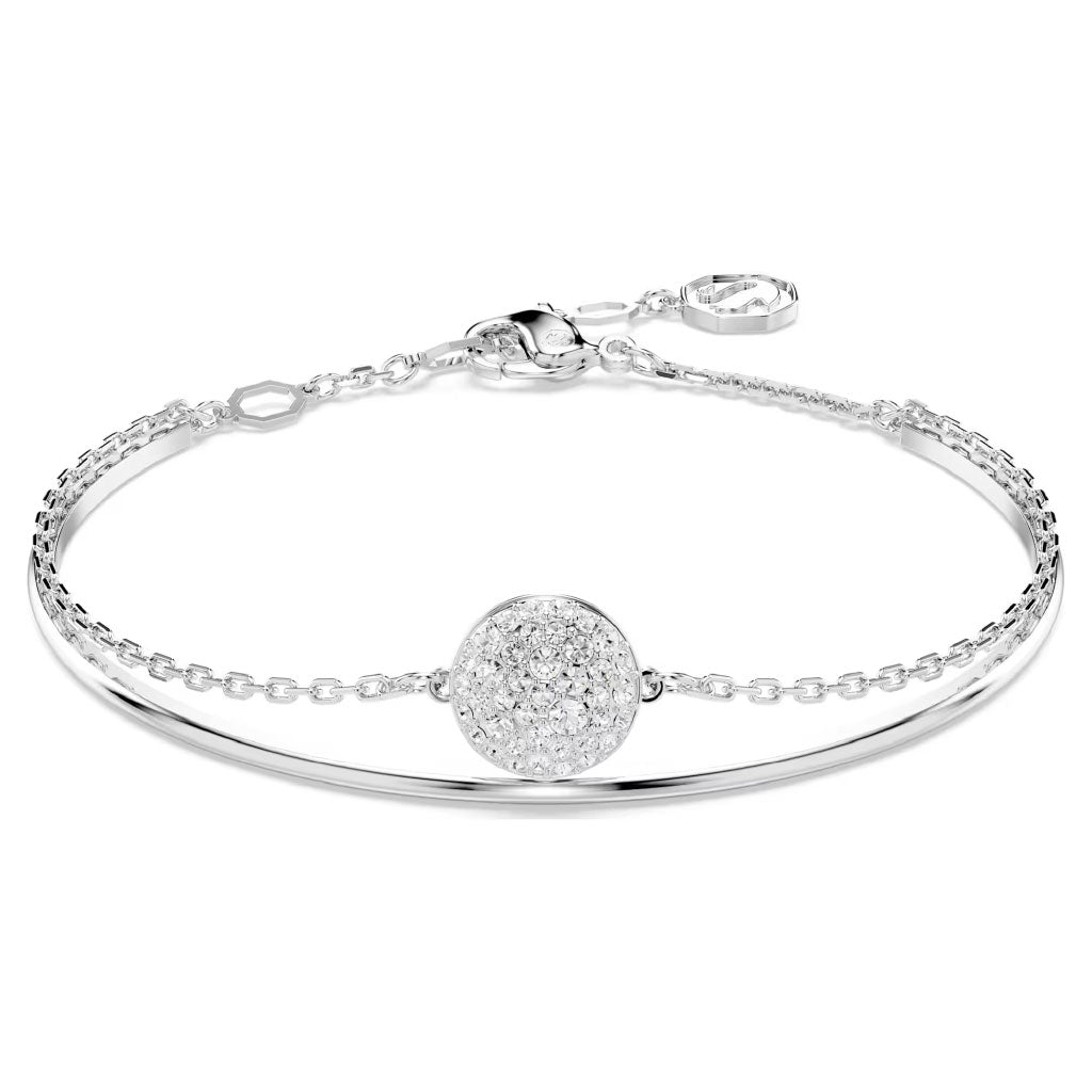 The Swarovski Sublima Bangle by Swarovski showcases a delicate silver bracelet with a circular, textured charm adorned with small crystals. This rhodium-plated piece features a slender chain and an adjustable clasp for fastening, offering an elegant and minimalistic design reminiscent of a starry bangle.