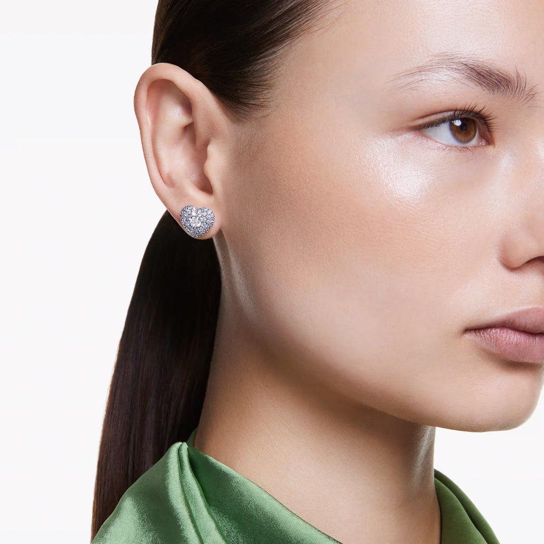 A close-up of a person wearing Swarovski Idyllia Stud Earrings. They have smooth skin and are dressed in a shiny green top, with their hair pulled back against a plain white background.