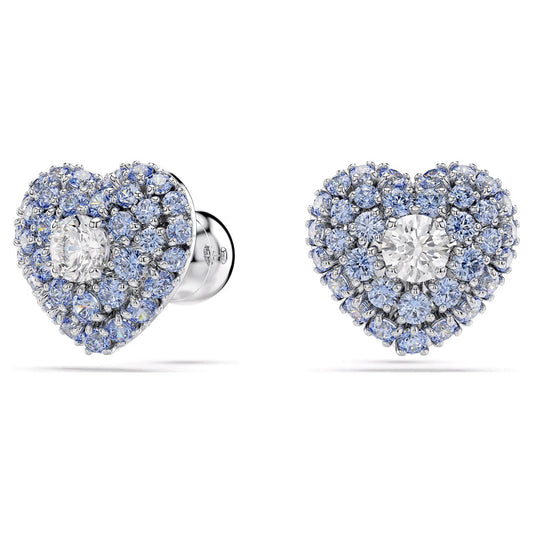 The Swarovski Idyllia Stud Earrings, crafted by Swarovski, feature heart-shaped designs with a central Swarovski Zirconia, encircled by smaller blue diamonds set in silver. These Rhodium-plated studs shine beautifully against a pristine white backdrop.