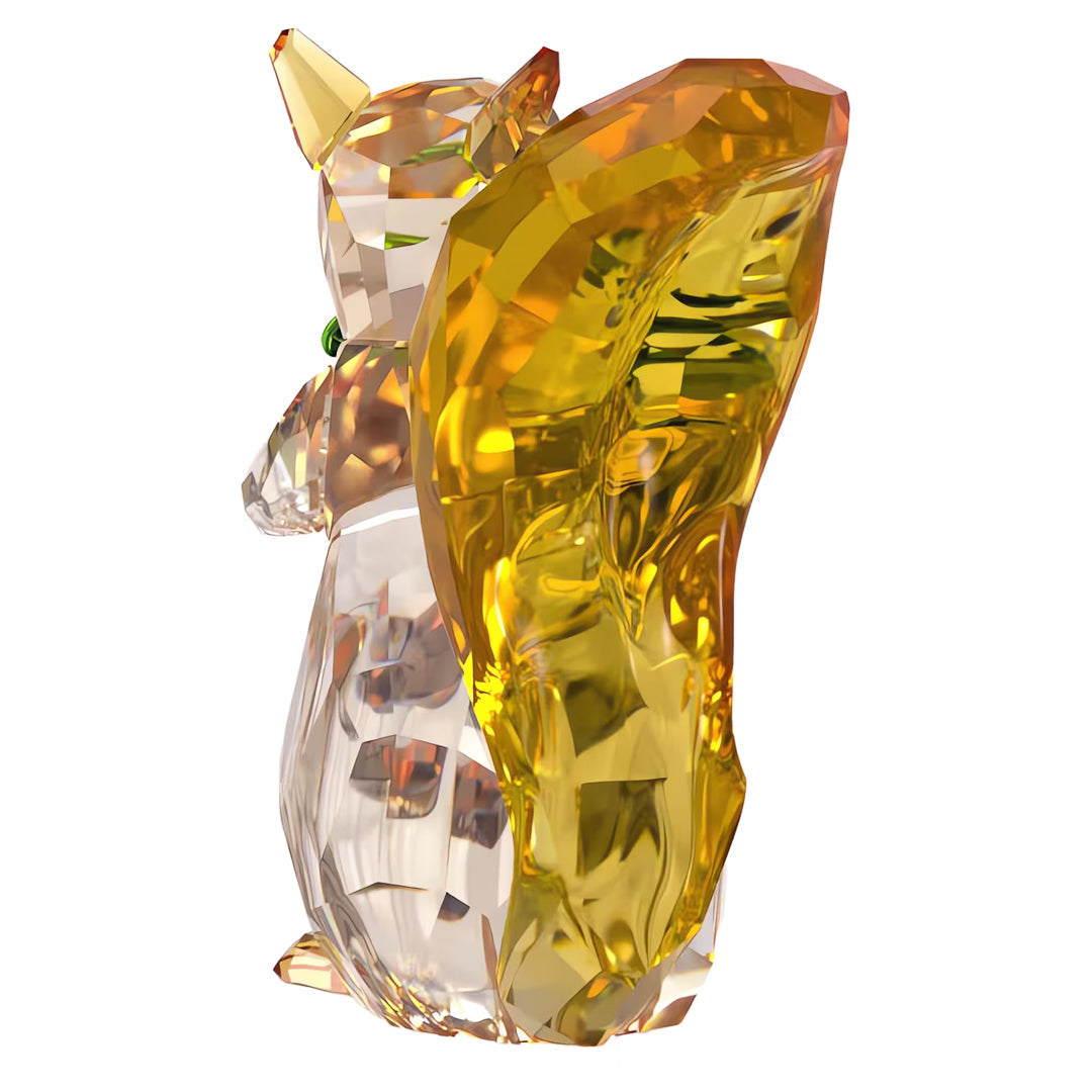 Introducing the Swarovski Idyllia Squirrel and Acorn Home Décor, a stunning crystal figurine adorned with green eyes and featuring an elegant, faceted design. While primarily transparent, this piece includes a striking amber-colored element that beautifully reflects light, making it an exquisite nature ornament reminiscent of a fox's graceful beauty.
