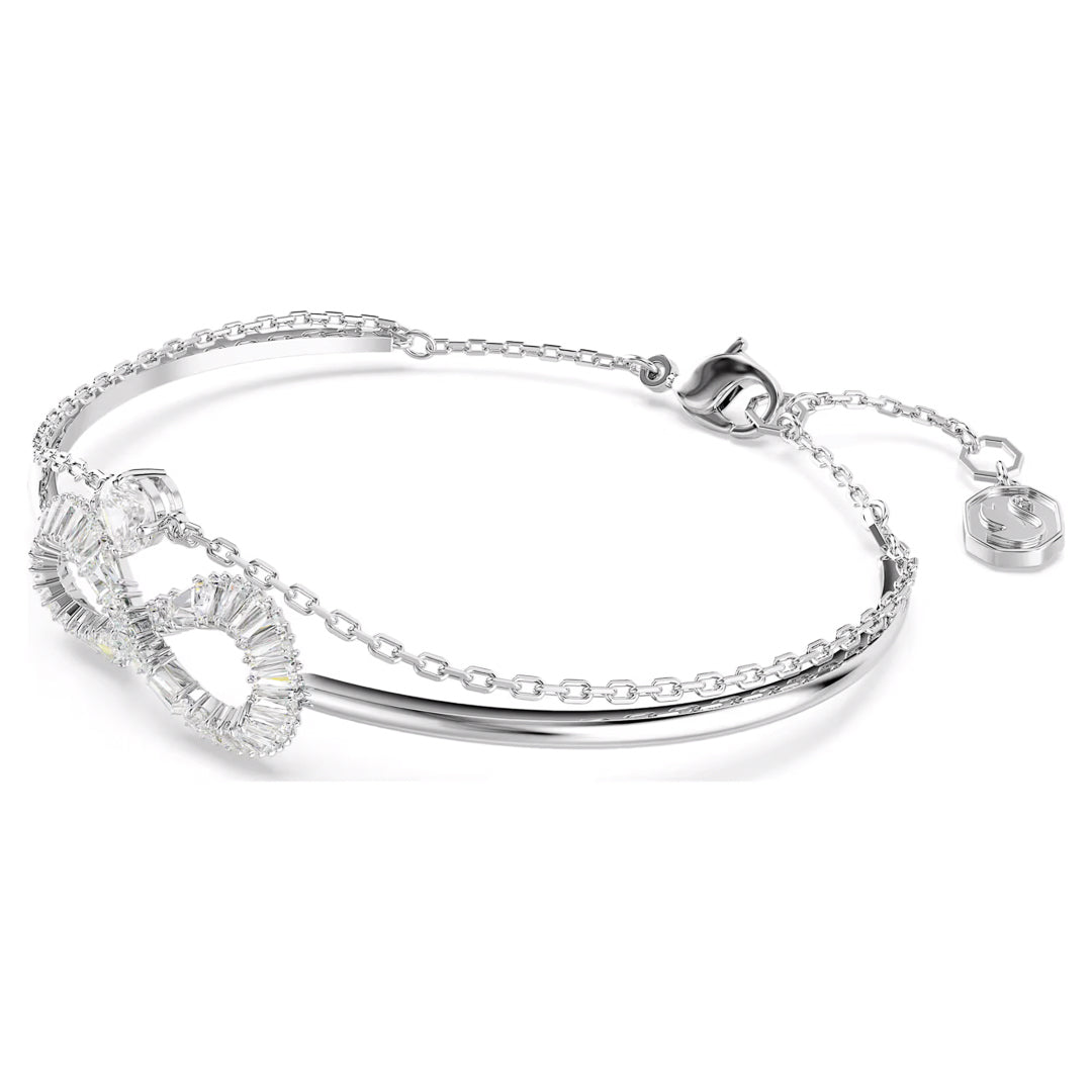 The Swarovski Hyerbola Bangle by Swarovski is an elegant and minimalist silver bracelet featuring a delicate rhodium-plated chain. It showcases a sparkling infinity symbol adorned with small Swarovski Zirconia crystals, along with a small charm near the adjustable clasp for a secure fit on the wrist.