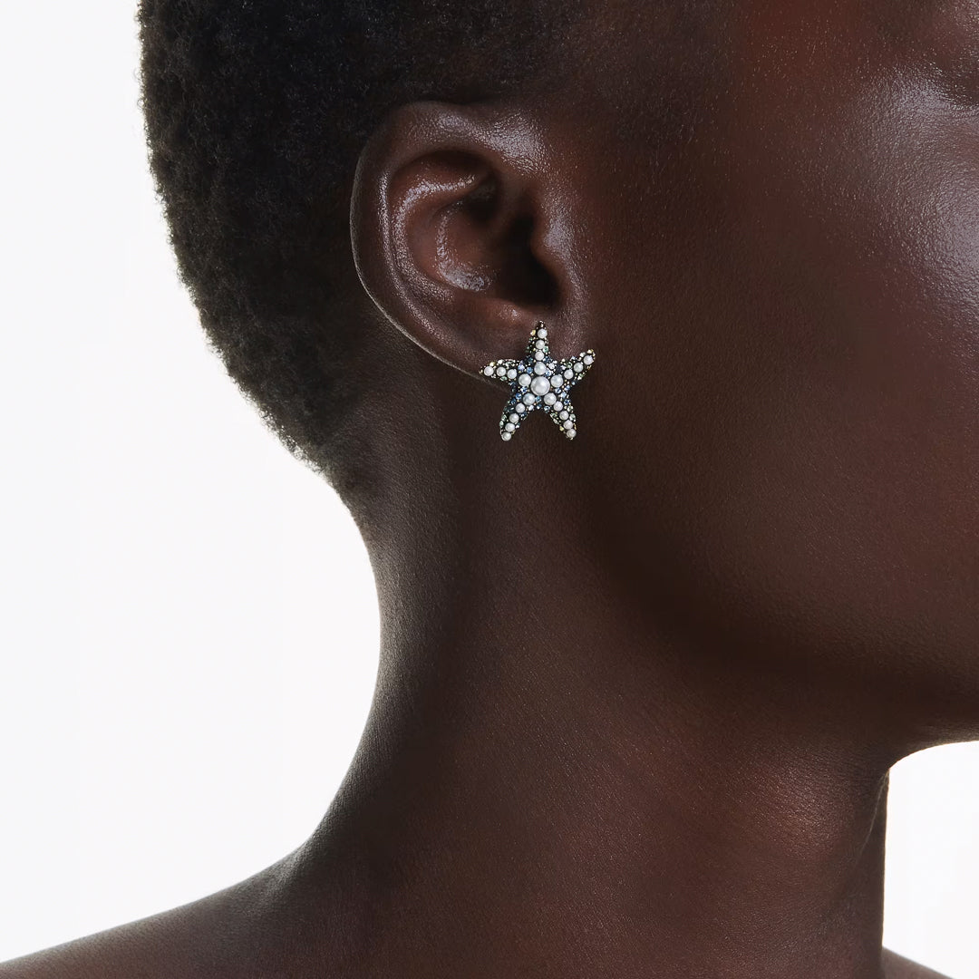 Close-up of a person wearing the Swarovski Idyllia Stud Earrings, which are ocean-inspired and starfish-shaped with small crystal pearls, set against a light background.