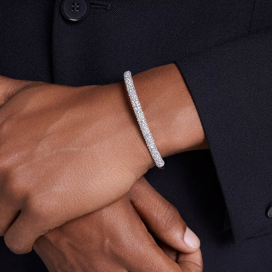 Close-up of a person wearing the elegant, silver Swarovski Sublima Bangle adorned with sparkling clear round crystals on their wrist. The rhodium-plated band shines brightly against the dark jacket as their hand gently rests on their forearm.