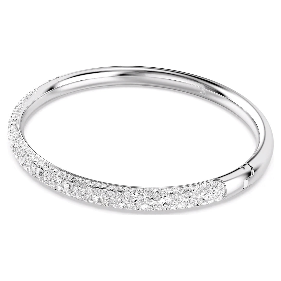 The Swarovski Sublima Bangle, crafted by Swarovski, is a sleek silver piece that features multiple sparkling diamonds encrusted along part of its circumference. The rhodium-plated band is set against a plain white background, emphasizing its elegant and luxurious design.