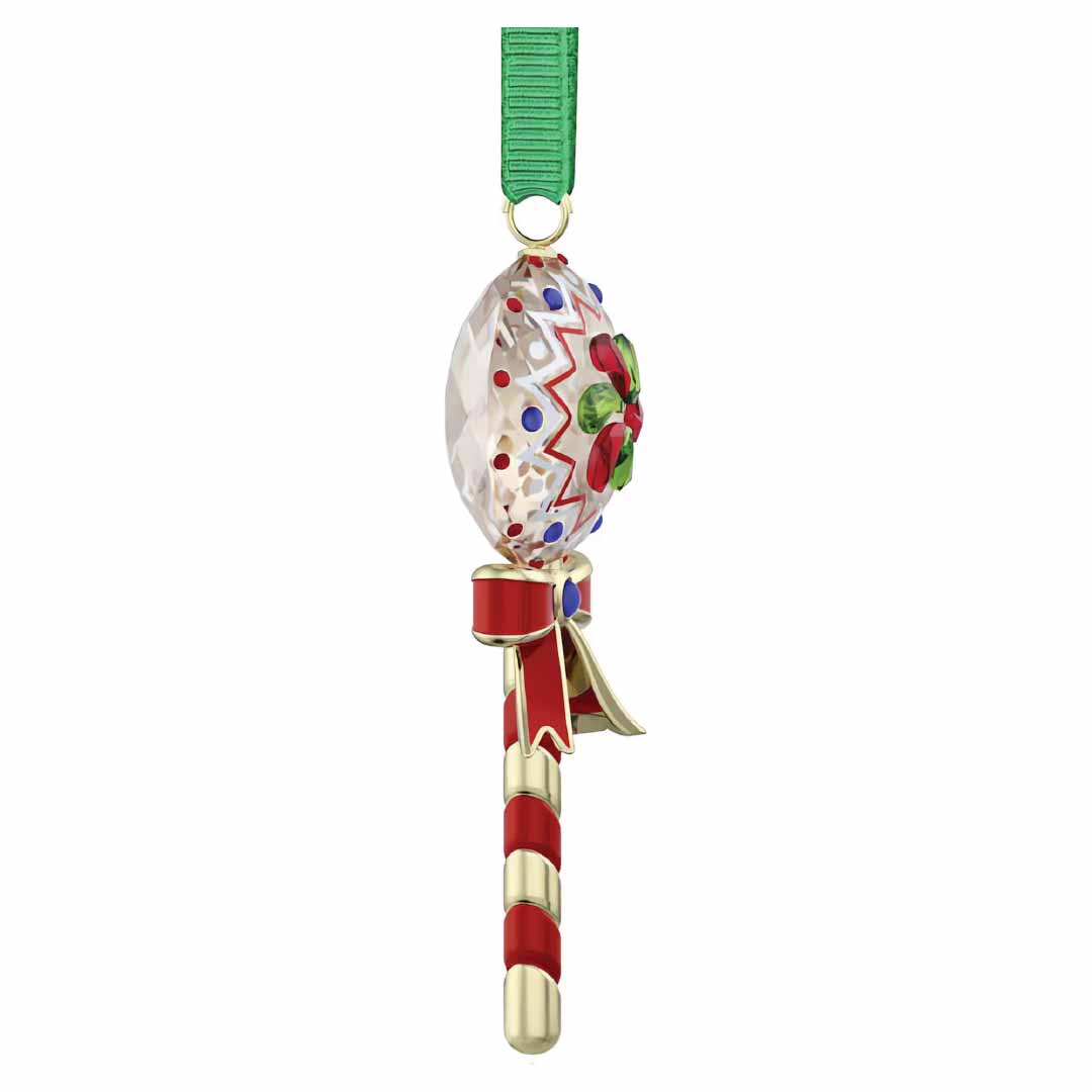 The Swarovski Holiday Cheers Dulcis Lollipop Ornament by Swarovski is a festive decoration designed in the shape of a crystallized lollipop ornament. It showcases a clear, oval top with intricate red, green, and blue patterns. The gold and red striped stem is complemented by a decorative red bow. Featuring an attached green ribbon for easy hanging, this ornament makes an ideal holiday gift.