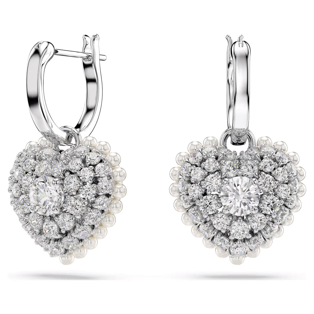 The Swarovski Hyperbola Heart Drop Earrings, by Swarovski, feature a rhodium-plated heart design adorned with sparkling Swarovski Zirconia and delicate pearls, centered around a large diamond. With hoop clasps for fastening, these earrings exude elegance and sophistication against a white background.