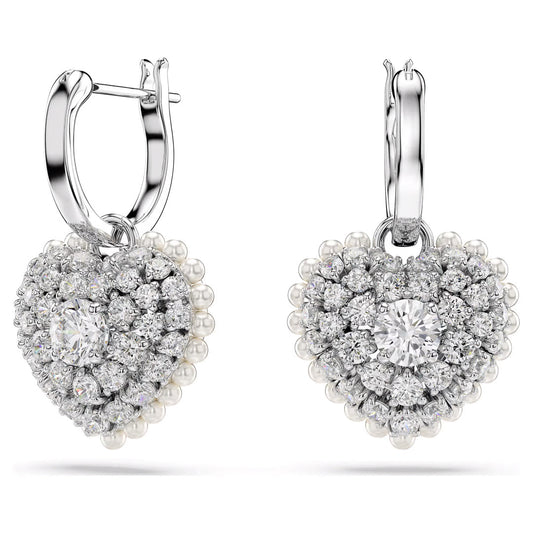 The Swarovski Hyperbola Heart Drop Earrings, by Swarovski, feature a rhodium-plated heart design adorned with sparkling Swarovski Zirconia and delicate pearls, centered around a large diamond. With hoop clasps for fastening, these earrings exude elegance and sophistication against a white background.