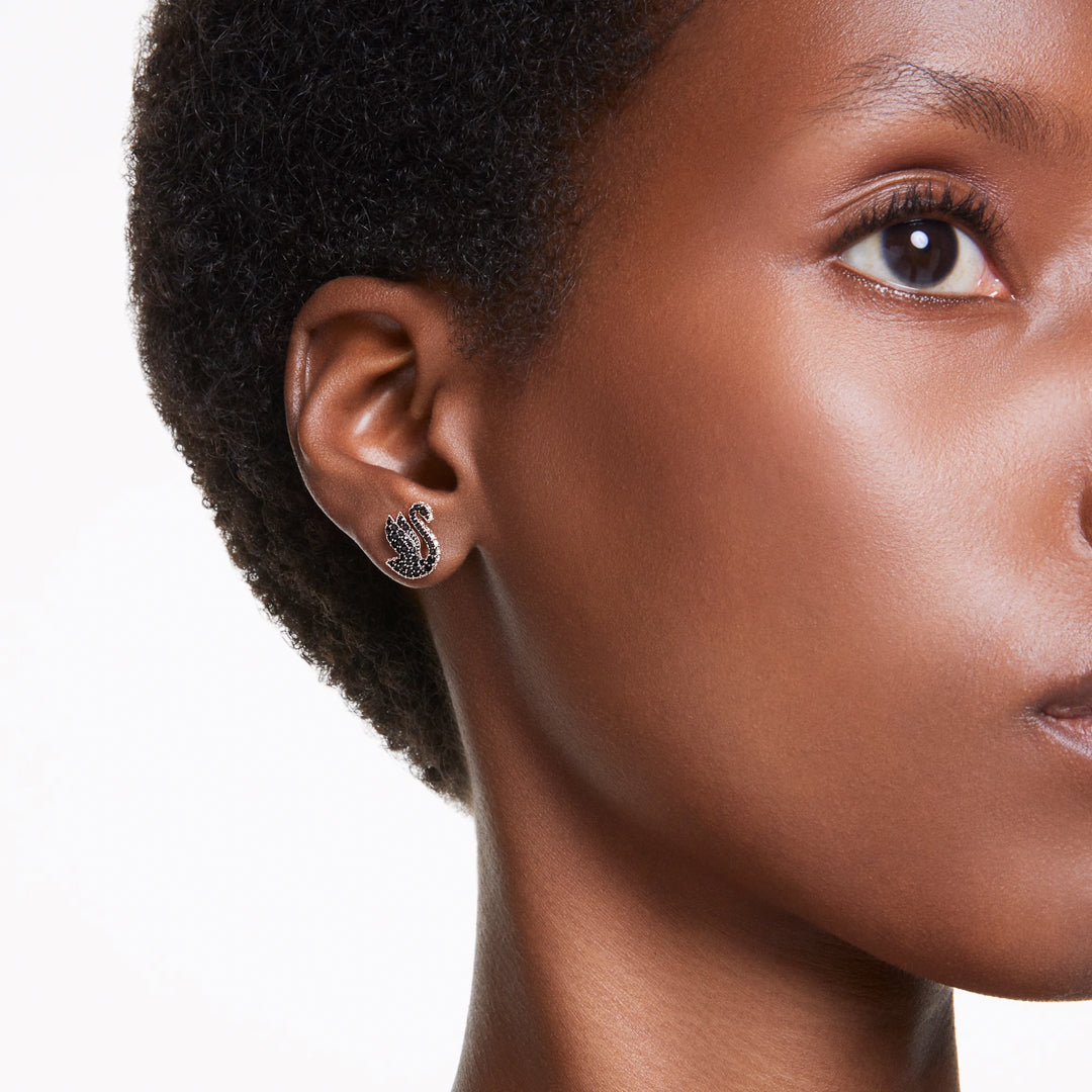 Close-up of a person wearing the Swarovski Swan Stud Earring on their left ear. The earring features a rose gold-tone finish with embedded gemstones, showcasing the elegance of Crystal Pearl accents against a plain white background.