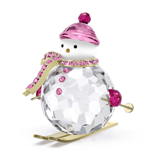 The Swarovski Holiday Cheers Dulcis Snowman Home Décor features a faceted crystal snowman made with sparkling Swarovski crystals and accented in pink. This charming figure, wearing a pink beanie and scarf, balances gracefully on skis embellished with gold details, infusing any space with a cheerful winter wonderland charm.