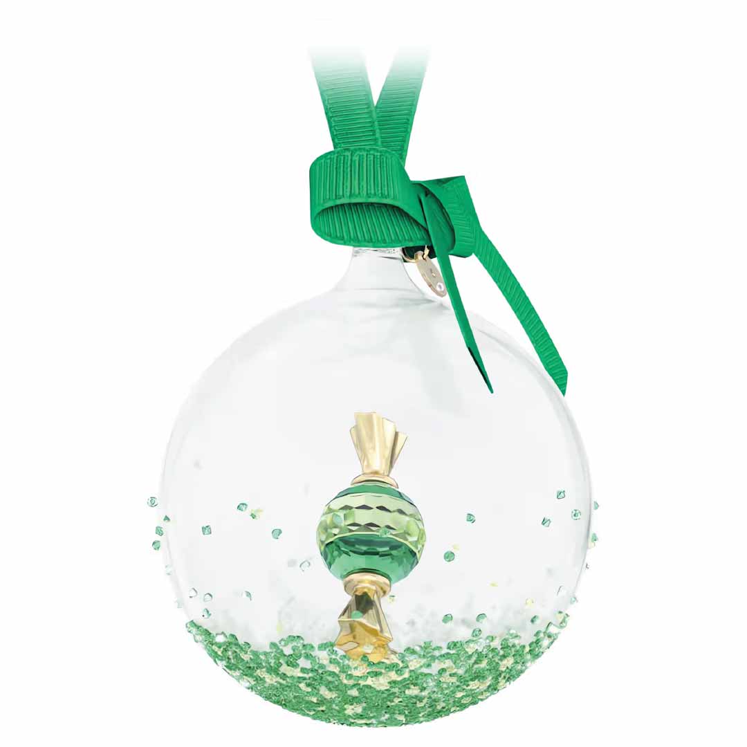 The Swarosvki Holiday Cheers Dulcis Ball Ornament Home Décor from Swarovski features a small green and gold candy replica encased in a clear decorative ornament, surrounded by gleaming crystal rocks. Elegantly suspended by a green ribbon, this design embodies the enchanting charm characteristic of Swarovski ball ornaments.