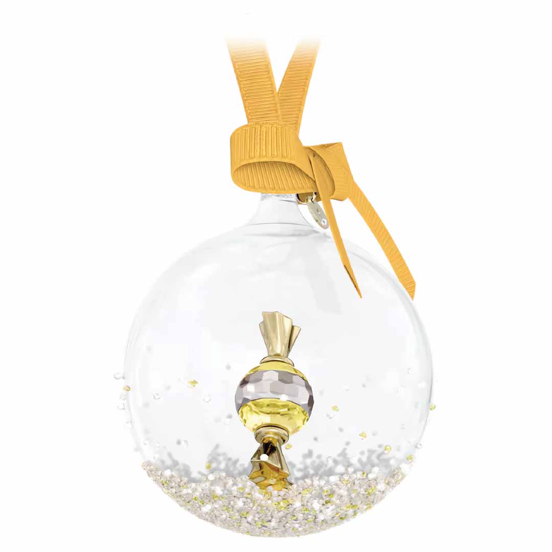 The Swarovski Holiday Cheers Dulcis Bell Ornament Home Décor features a transparent glass design encasing a gleaming gold candy and topped with elegant gold ribbon. Its base is adorned with tiny, sparkling beads, reminiscent of a classic Swarovski ball ornament, adding dazzling charm to your collection.