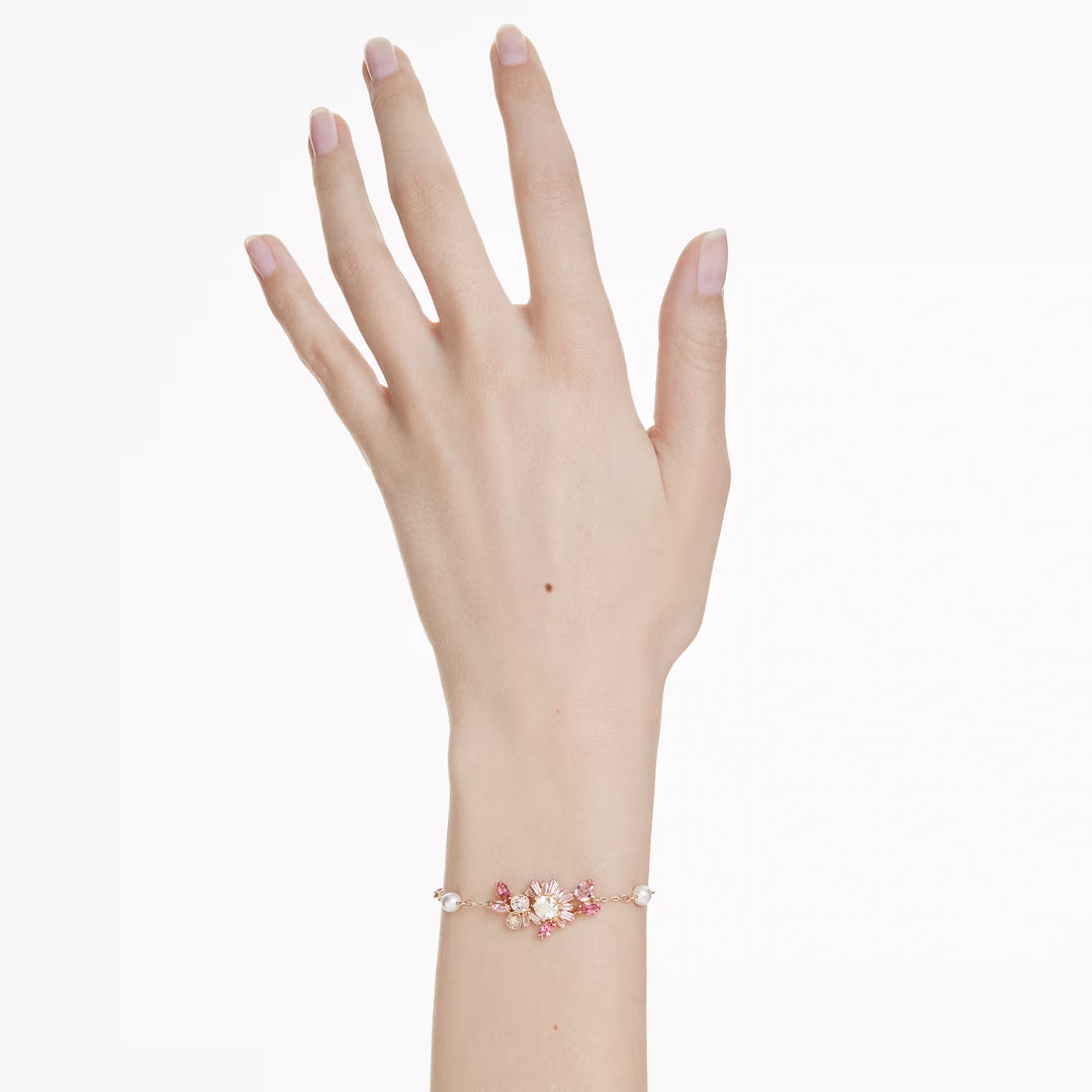A delicate Swarovski Gema Bracelet graces a person's wrist, showcasing pink and white floral designs accented with sparkling Swarovski Zirconia. The hand is elegantly posed against a plain white background.