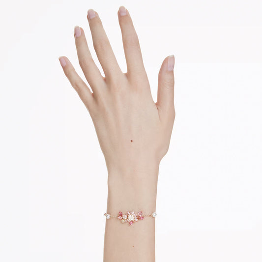 A delicate Swarovski Gema Bracelet graces a person's wrist, showcasing pink and white floral designs accented with sparkling Swarovski Zirconia. The hand is elegantly posed against a plain white background.