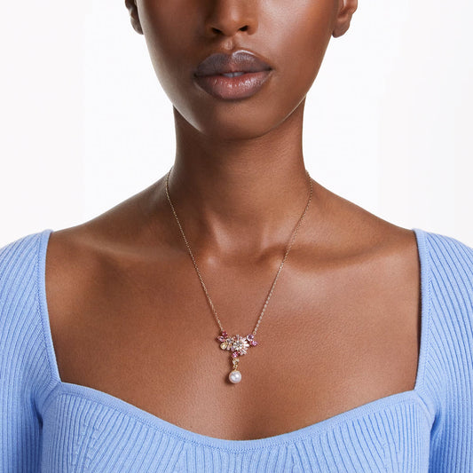 A person wearing a light blue, off-the-shoulder top and the elegant Swarovski Gema Necklace Pendant by Swarovski, featuring sparkling Swarovski Zirconia and a hanging pearl. The background is plain white.