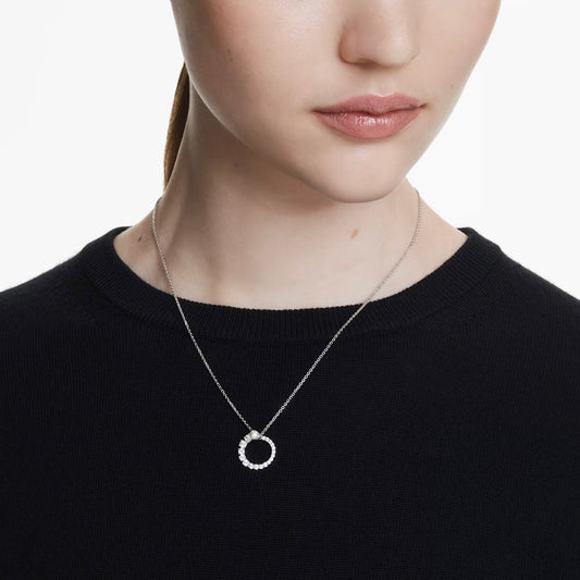 A person wearing a black sweater and a Swarovski Matrix Necklace Pendant. The image captures the lower face and upper chest, emphasizing the intricate design of this Swarovski jewelry. The plain white background accentuates the elegance of the piece.