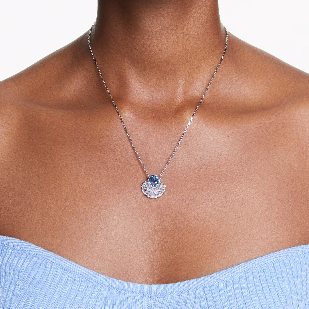 A person wearing the Swarovski Idyllia Necklace Pendant, a delicate silver piece featuring a marine-inspired charm adorned with a blue Swarovski Zirconia. The seashell-shaped pendant perfectly complements the light blue, strapless, textured top against a simple white background that enhances the elegance of this stunning ensemble.