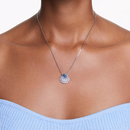 A person wearing the Swarovski Idyllia Necklace Pendant, a delicate silver piece featuring a marine-inspired charm adorned with a blue Swarovski Zirconia. The seashell-shaped pendant perfectly complements the light blue, strapless, textured top against a simple white background that enhances the elegance of this stunning ensemble.