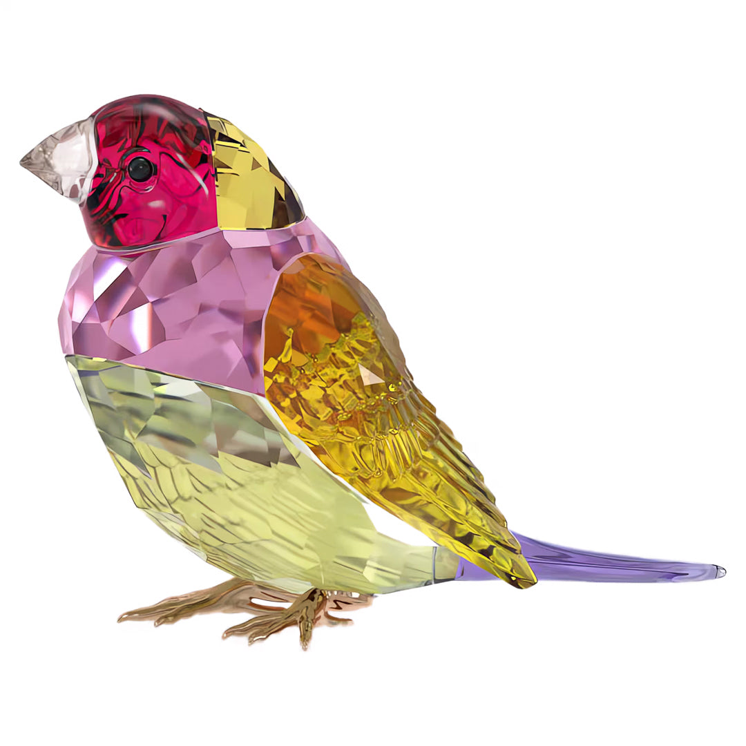 This vibrant decoration, the Swarovski Idyllia SCS Gouldian Finch Home Décor figurine by Swarovski, showcases a pink head, yellow breast, and purple tail. Its body features shades of orange and green with detailed craftsmanship that sparkles brilliantly like classic Swarovski crystals.