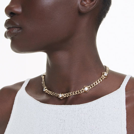 A person wearing the Swarovski Numia Necklace, a stunning piece from Swarovski featuring gold-tone plating with pearl accents and industrial-style elements. The individual is dressed in a white sleeveless top against a plain background.
