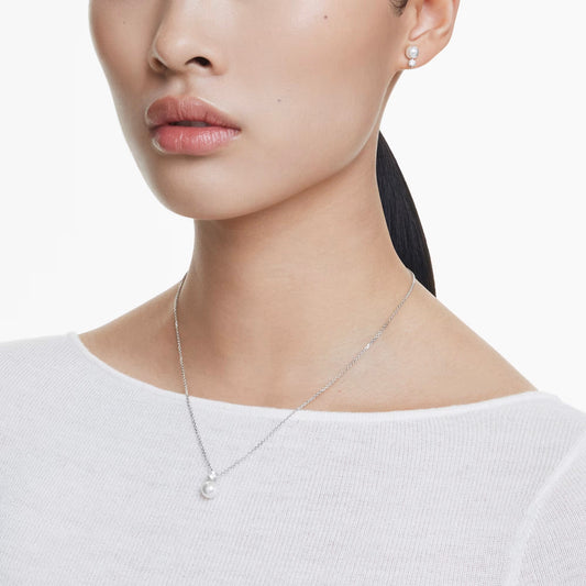 A person adorned in a white top pairs their dark, tied-back hair with the elegant Swarovski Matrix Earrings and Necklace Set. The silver necklace features a Swarovski Crystal Pearl pendant and is accompanied by matching pearl earrings, both accentuated by rhodium-plated details that stand out against the plain white background.