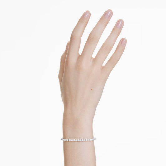 A hand with neatly manicured nails is adorned with a delicate Swarovski Matrix Bracelet, featuring small Swarovski Crystal Pearls. The plain white background accentuates the hand and bracelet.