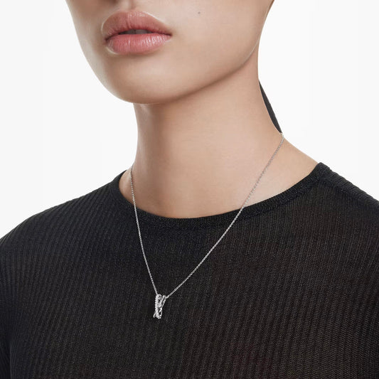A person is adorned in a ribbed black top paired with the Swarovski Hyperbola Necklace Pendant, skillfully crafted from the elegant Hyperbola collection. This letter-shaped pendant by Swarovski adds a touch of sophistication against the pristine white backdrop.