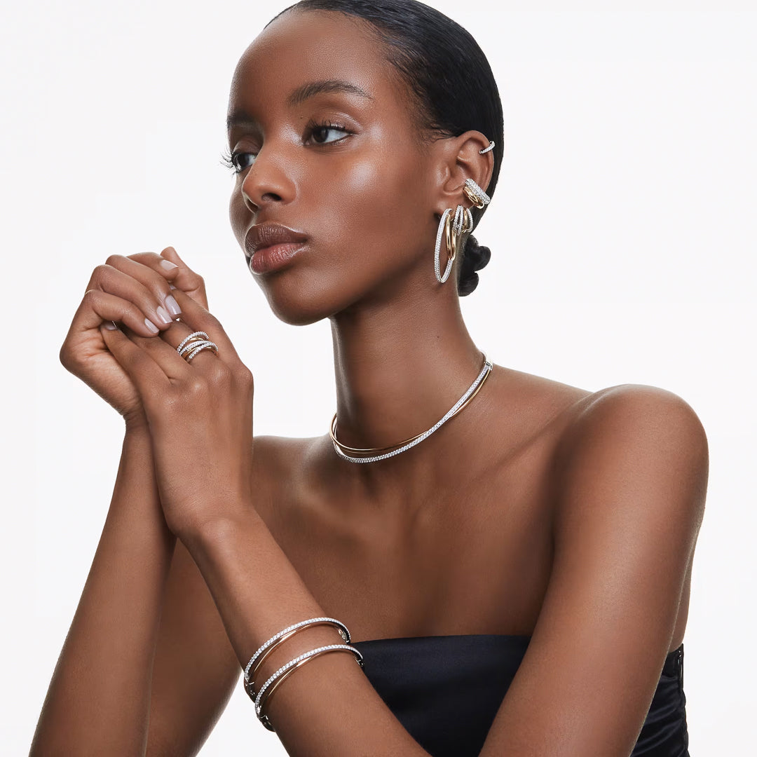 A woman wearing a strapless black top accessorized with silver jewelry, including the sparkling Swarovski Matrix Hoop Earrings, a necklace, rings, and bracelets. She is gazing to the side against a plain white background.