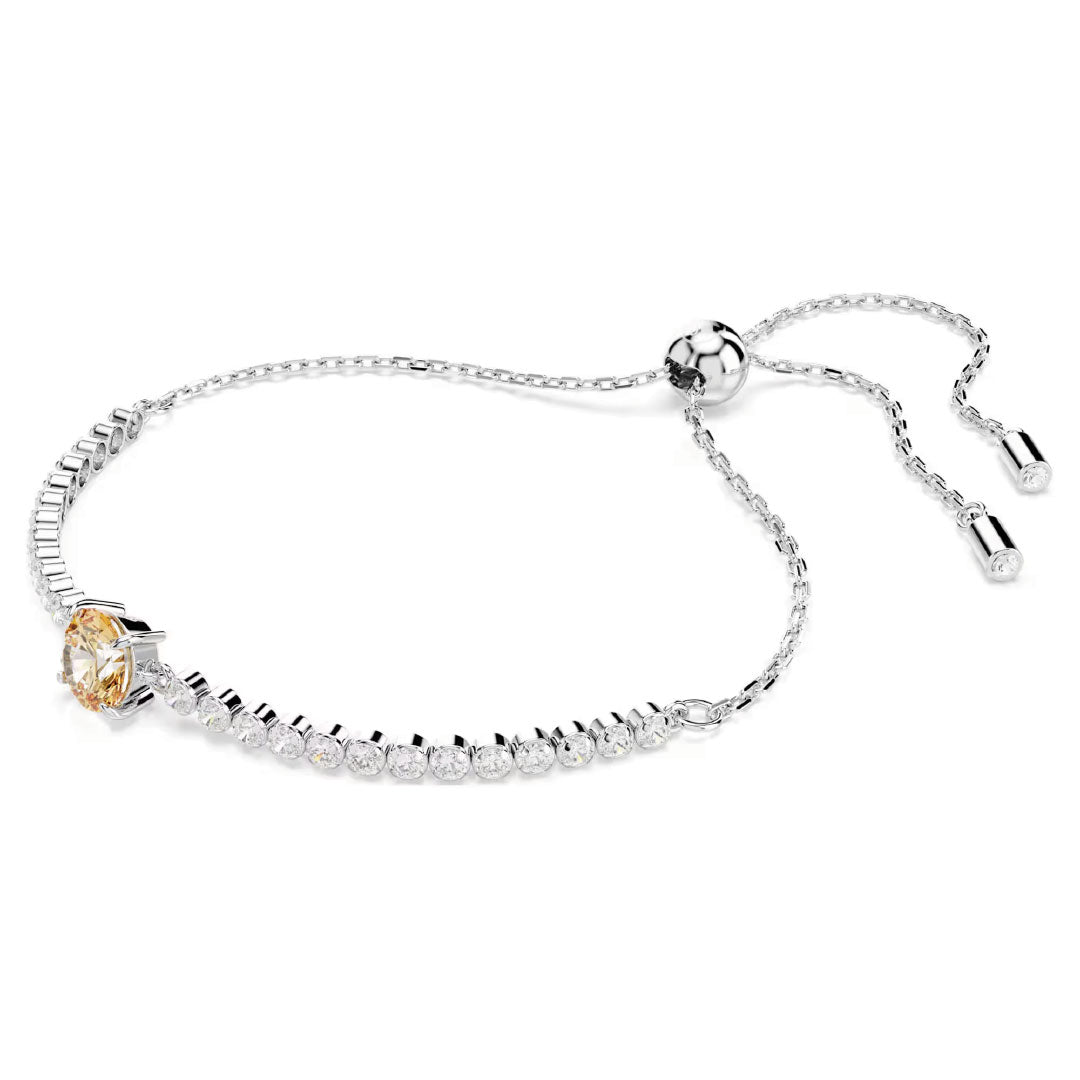 The Swarovski Matrix Tennis Bracelet, crafted by Swarovski, is a rhodium-plated silver piece featuring an adjustable chain adorned with a cluster of round, sparkling diamonds. The design boasts a central gemstone with a radiant yellow hue, offering an elegant and luxurious look akin to that of a classic tennis bracelet.