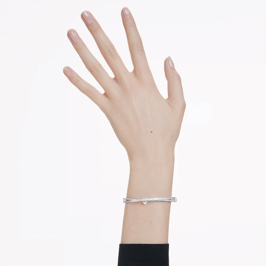 A hand with a light skin tone showcases the Swarovski Hyperbola Bangle, a rhodium-plated bracelet shaped like a miniature nail. The manicured nails are adorned with light pink polish, all set against a plain white background.