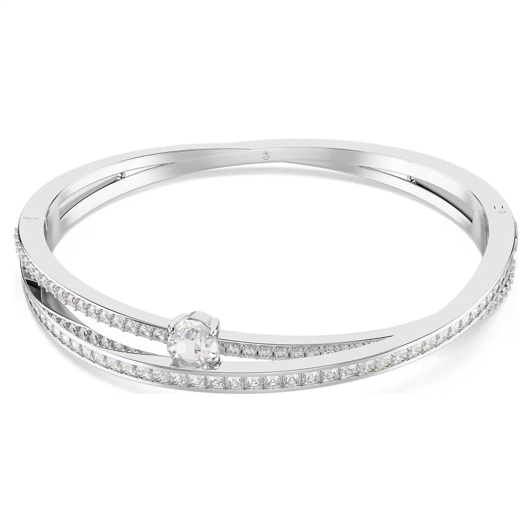 The Swarovski Hyperbola Bangle by Swarovski is a sleek rhodium-plated silver piece featuring two parallel bands. One band is adorned with small, sparkling Swarovski Zirconia stones, while the other showcases a prominent central gemstone. This elegant and modern design captures light beautifully to enhance its brilliance.