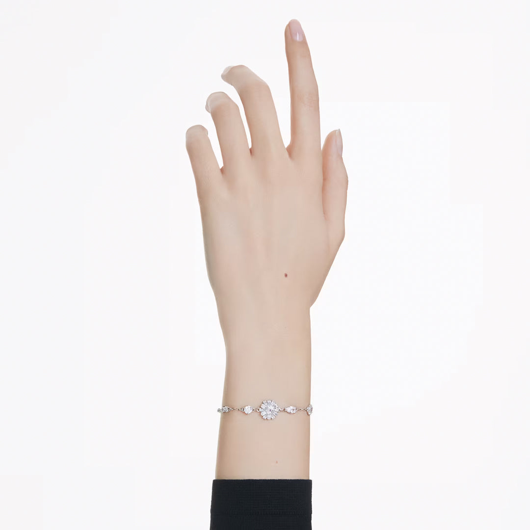 A delicate hand gracefully reaches upward, adorned with the Swarovski Idyllia Bracelet on the wrist. This rhodium-plated piece by Swarovski beautifully showcases a central, oval-shaped diamond surrounded by smaller diamonds and Swarovski Zirconia in a snowflake motif, all set against a simple black sleeve backdrop.