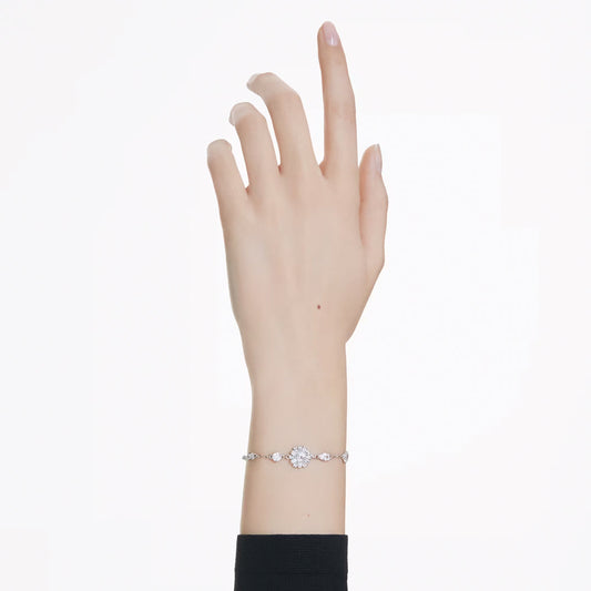 A delicate hand gracefully reaches upward, adorned with the Swarovski Idyllia Bracelet on the wrist. This rhodium-plated piece by Swarovski beautifully showcases a central, oval-shaped diamond surrounded by smaller diamonds and Swarovski Zirconia in a snowflake motif, all set against a simple black sleeve backdrop.
