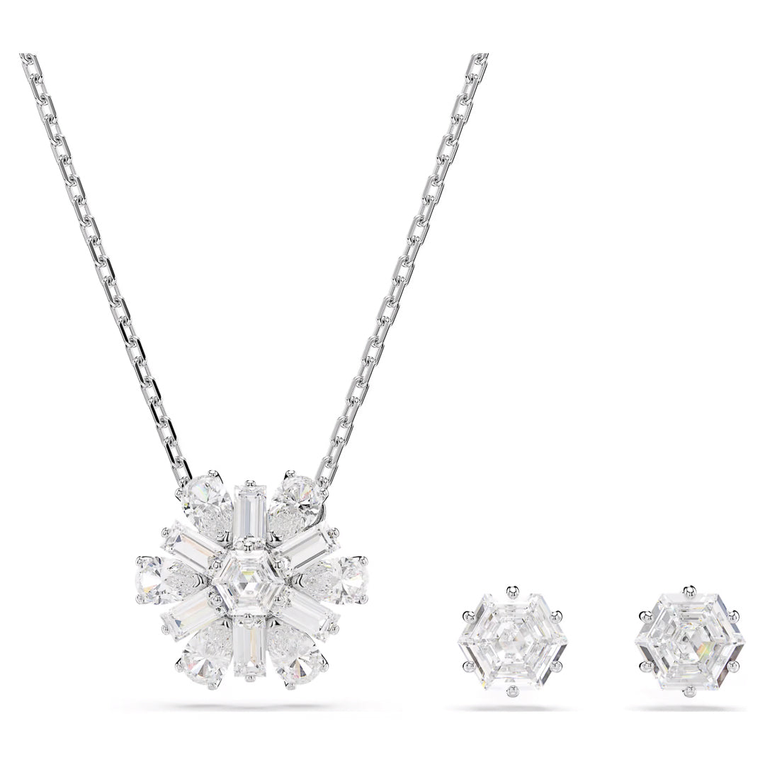 The Swarovski Idyllia Necklace and Earrings Set by Swarovski includes a silver chain necklace with a snowflake-shaped pendant adorned with variously cut clear stones, brilliantly enhanced by sparkling Swarovski Zirconia. Accompanying the necklace is a pair of matching hexagonal stud earrings, also embellished with clear stones, glistening against a white background.