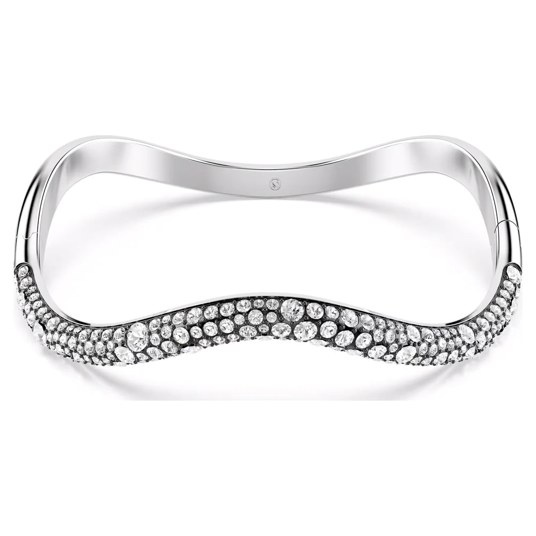 The Swarovski Sublima Bangle showcases a wave-inspired design, enhanced with ruthenium plating for a touch of elegance, and adorned with numerous small, sparkling gemstones that produce a shimmering effect across its surface.