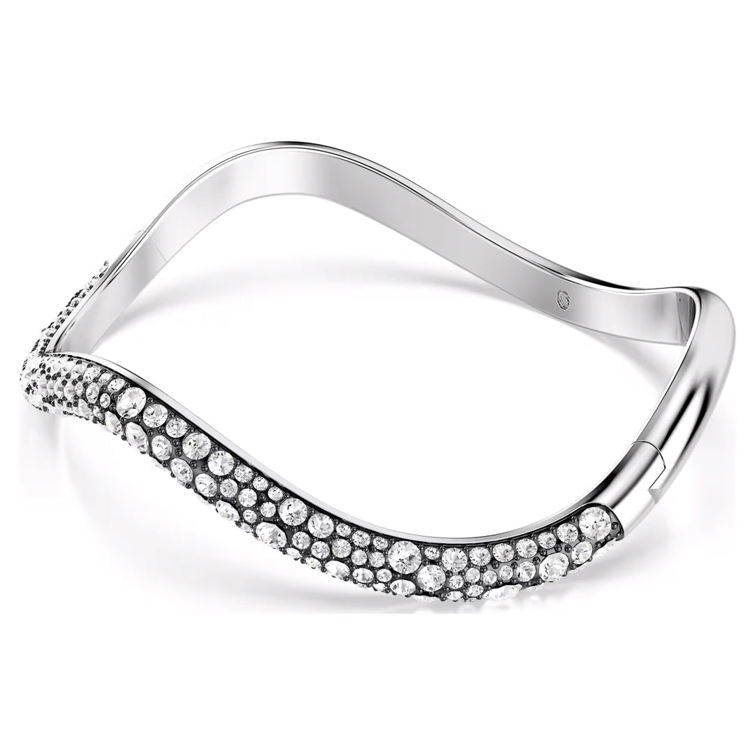 The Swarovski Sublima Bangle, crafted by Swarovski, is a chic silver bracelet featuring a contemporary undulating wave design. Enhanced with rhodium plating for extra sophistication, it is embellished with clear crystals in varying sizes that together create an effortlessly stylish appearance.
