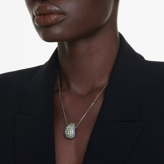 A person wearing a black blazer showcases the Swarovski Sublima Necklace Pendant, adorned with crystals in silver and marine-inspired shades. The close-up captures the elegance and intricate details of the jewelry, while the plain white background emphasizes the necklace's beauty.