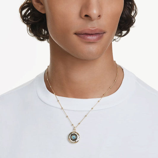 A person wearing a white t-shirt and the Swarovski Symbolica Necklace Pendant, which features a gold-tone plated eye design. The plain white background highlights the unique details of this elegant piece by Swarovski.