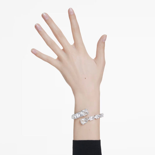 A hand with neatly manicured nails is raised against a white background, elegantly adorned with the Swarovski Matrix Bangle, rhodium plated and encrusted with clear crystals.
