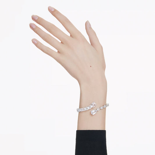 A hand model with impeccably manicured nails showcases the Swarovski Matrix Cuff, a rhodium-plated bracelet adorned with diamonds and clear crystals, set against a simple white backdrop. The cuff boasts an elegant open-ended design with teardrop-shaped ends.