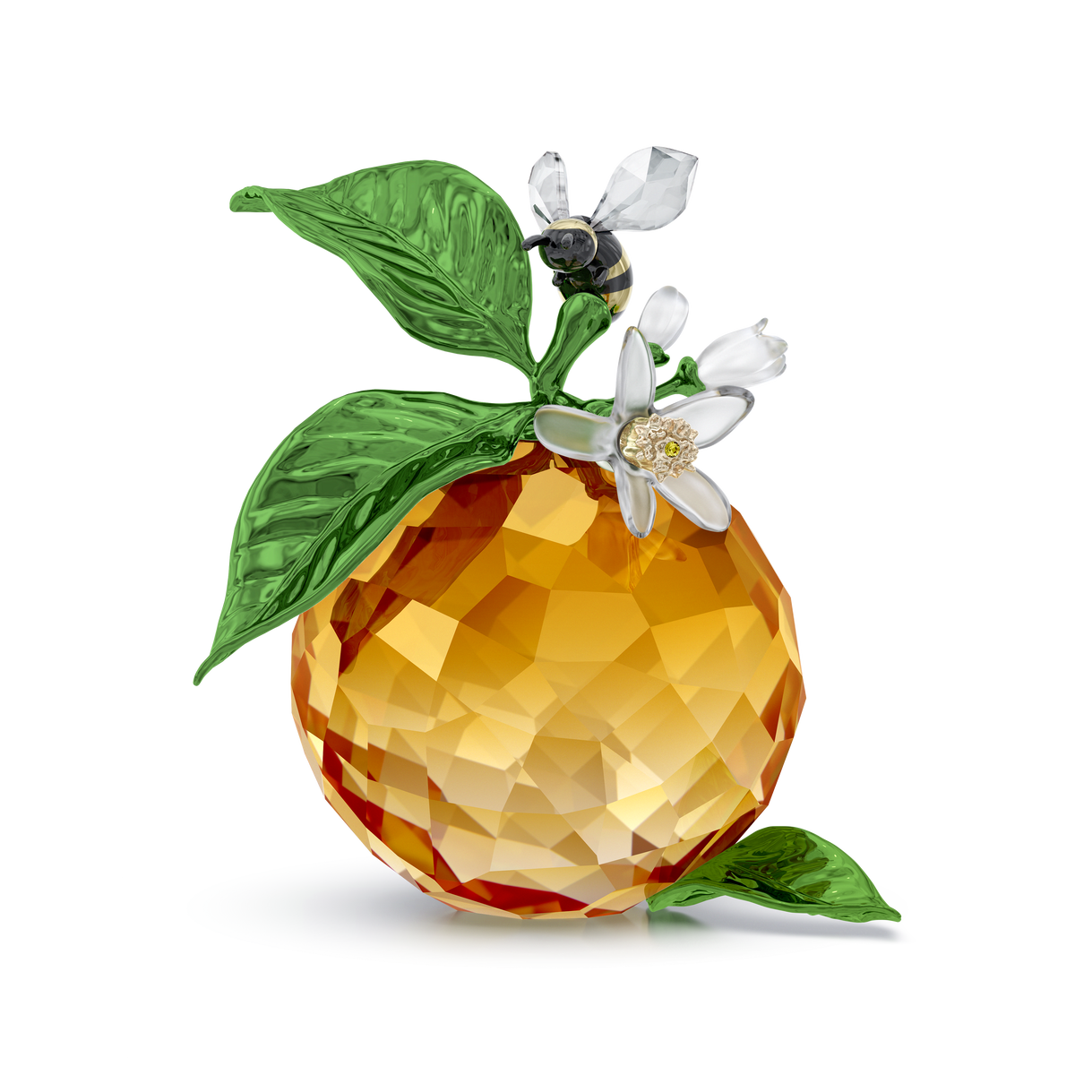 The Swarovski Idyllia Clementine and Bee by Swarovski features faceted crystal orange with green crystal leaves, delicate white crystal blossoms, and a small Swarovski Idyllia crystal bee figurine perched atop the blossom, set against a plain white background.