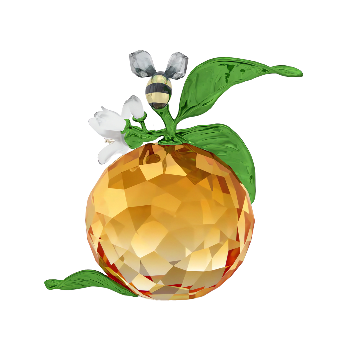 A faceted orange crystal, evocative of a decorative clementine, is accented with green leaves and crowned by a delicate glass bee and white flower—showcasing the exquisite craftsmanship of the Swarovski Idyllia Clementine and Bee figurine by Swarovski—set against a plain white background.