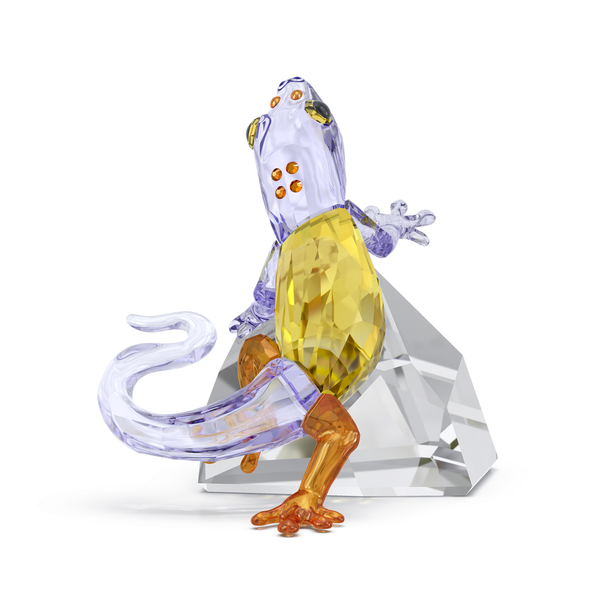 The Swarovski Idyllia Gecko by Swarovski features a glass lizard figurine with a yellow body, purple head and tail, and orange legs, posed on a clear geometric glass base against a white background—making it a striking crystal decoration or home centerpiece.