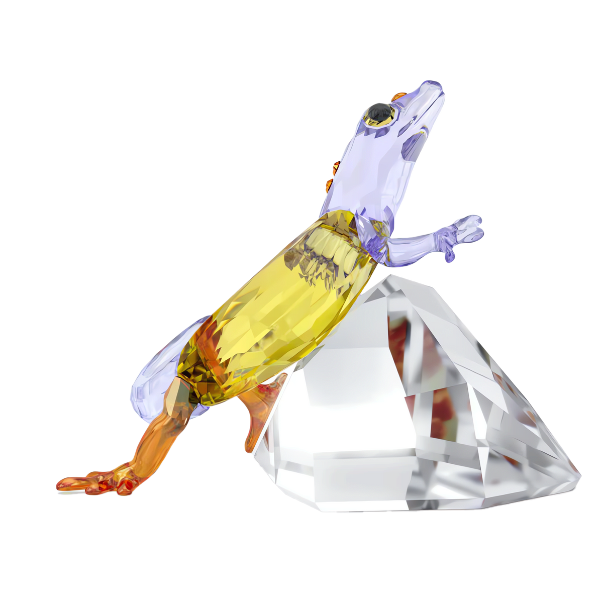 The Swarovski Idyllia Gecko by Swarovski features a vibrant glass sculpture with yellow, orange, and purple hues climbing a faceted clear crystal rock against a plain white background—creating a striking gecko figurine and eye-catching crystal decoration for any home centerpiece.