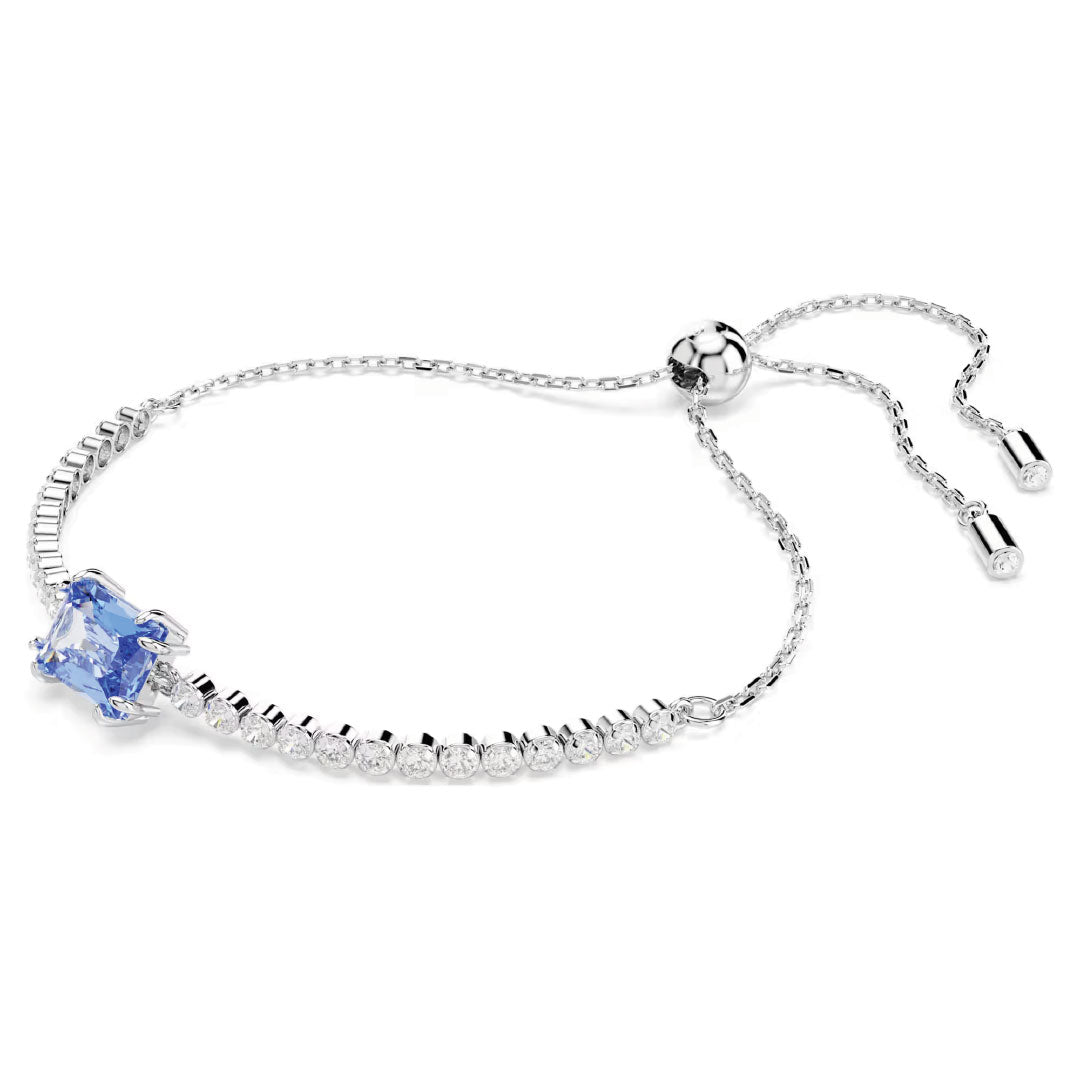 The Swarovski Matrix Tennis Bracelet by Swarovski features a series of small, round white Swarovski Zirconia leading to a larger blue gemstone centerpiece and includes an adjustable chain with two delicately dangling elements.