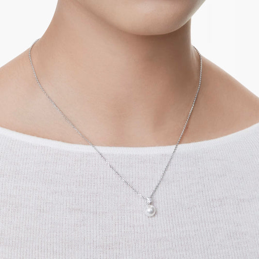 A person wearing the Swarovski Matrix Necklace Pendant, featuring a simple silver chain adorned with a Swarovski Crystal Pearl, is dressed in a white off-the-shoulder top that highlights their neck and collarbone against a plain backdrop.