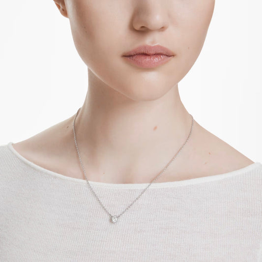 Against a plain white background, an individual wears the Swarovski Imber Necklace Pendant, an elegant silver piece featuring a small pendant delicately enhanced with Swarovski Zirconia. The person is dressed in a light-colored, textured top, with only the lower half of the face and neck visible.