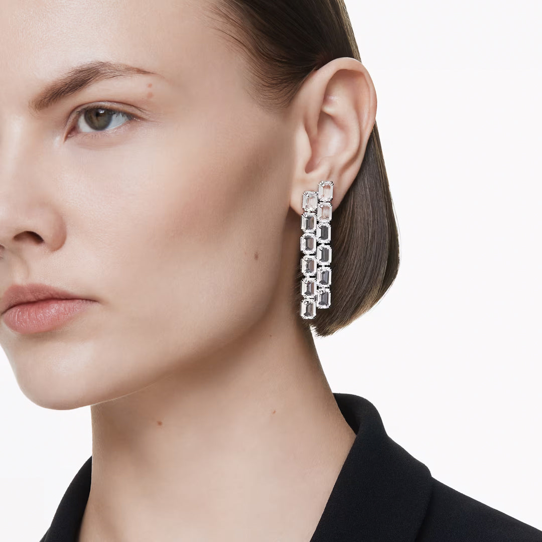 A person is shown from the side wearing a black top, with their ear adorned by the striking Swarovski Millenia Clip Earrings featuring octagon-cut crystals. The plain white background enhances the earring's bold design.